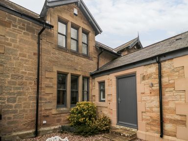 Exterior view of a stone house with windows a gray door and plants in front at Grange Cottages in Alnwick