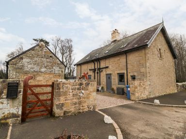 Stone house with slate roof and small wooden gate in front at Grange Cottages in Alnwick