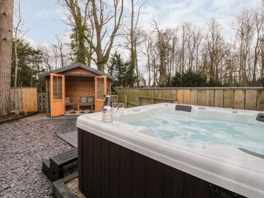 An outdoor area with a hot tub and a wooden shed with seating at Grange Cottages in Alnwick