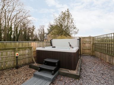 An outdoor hot tub with steps on gravel surrounded by wooden fencing at Grange Cottages in Alnwick