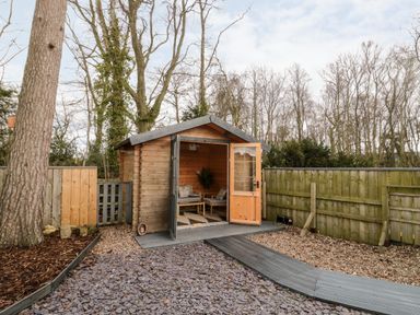 A wooden garden shed with open doors and chairs inside surrounded by gravel and a wooden fence at Grange Cottages in Alnwick