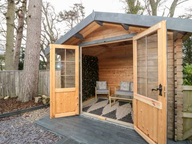 An outdoor wooden cabin with open double doors two chairs and a coffee table inside at Grange Cottages in Alnwick