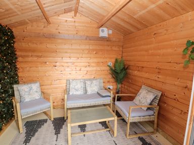 A small wooden room with a sofa two armchairs a glass coffee table a rug and some plants at Grange Cottages in Alnwick