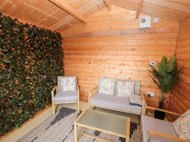 A wooden room with a wicker sofa and chairs with cushions a glass table a plant and a wall with decorative green leaves at Grange Cottages Alnwick