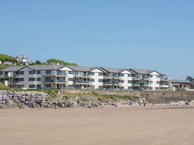 A sandy beach with people and umbrellas in front of apartment buildings at 17 Burgh Island Causeway in Bigbury-On-Sea
