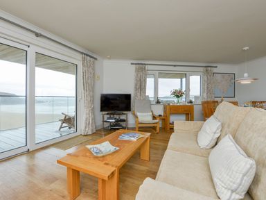 A living room with a sofa coffee table TV sliding glass doors showing a beach and balcony at 17 Burgh Island Causeway in Bigbury-On-Sea