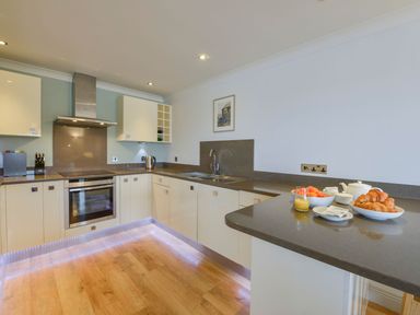 A kitchen with white cabinets a built in oven a sink and breakfast items on the counter at 17 Burgh Island Causeway in Bigbury-On-Sea