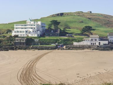 A sandy beach with tire tracks leading to buildings and green hills in the background at 17 Burgh Island Causeway in Bigbury-On-Sea