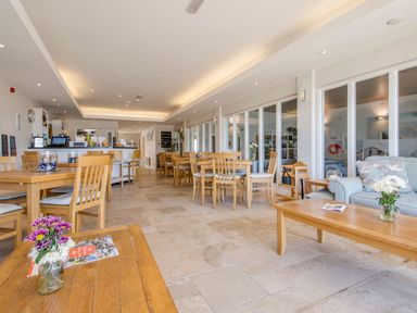 A dining area with wooden tables and chairs a service counter and a seating area with a sofa and a coffee table at 17 Burgh Island Causeway in Bigbury-On-Sea