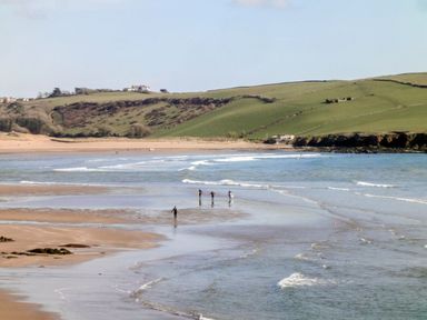 A beach with surfers walking on the wet sand and waves approaching on the shore at 17 Burgh Island Causeway in Bigbury-On-Sea