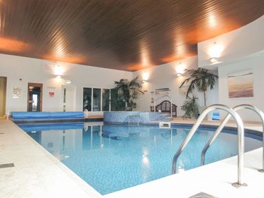 An indoor swimming pool with steps railing and plants along the walls at 17 Burgh Island Causeway in Bigbury-On-Sea