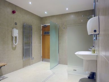 A tiled shower room with a frosted glass door wooden door hand dryer sink and metal towel rack at 17 Burgh Island Causeway in Bigbury-On-Sea