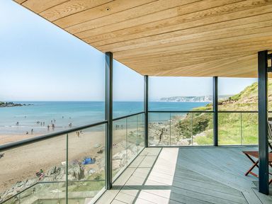 A balcony with glass railing overlooking a beach and ocean at 17 Burgh Island Causeway in Bigbury-On-Sea