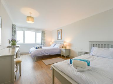 A bedroom with two beds bedside tables a dresser and a window with curtains at 17 Burgh Island Causeway Bigbury-On-Sea