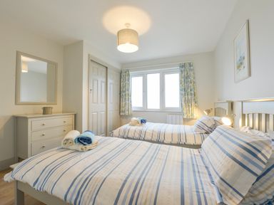 A bedroom with two single beds with striped bedding a chest of drawers and a window at 17 Burgh Island Causeway in Bigbury-On-Sea