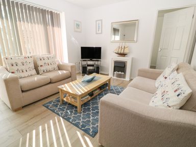 A living room with two beige sofas cushions with house patterns coffee table a TV on stand a wall mirror and a model ship at Ballasalla in Liskeard