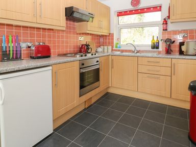 A kitchen with wooden cabinets red toaster and kettle and utensils on countertop at Ballasalla in Liskeard