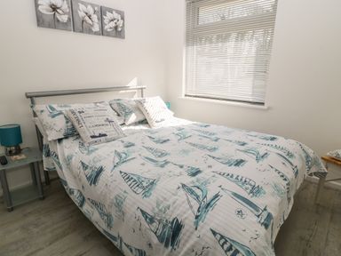A bedroom with a bed with boat-themed bedding a window with blinds two side tables with blue lamps and wall art with flowers at Ballasalla in Liskeard