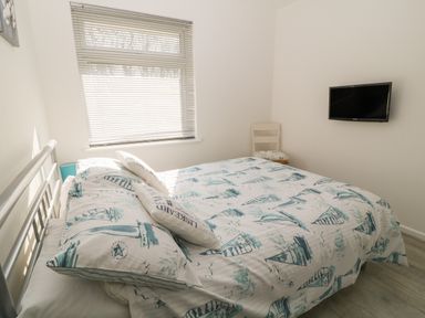 A bedroom with a bed with patterned bedding a chair in the corner and a wall-mounted television at Ballasalla in Liskeard