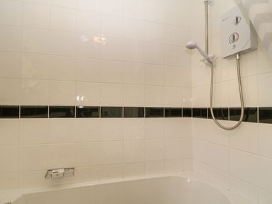 A bathroom with white tiled walls a black tile border a bathtub and a wall-mounted shower at Ballasalla in Liskeard
