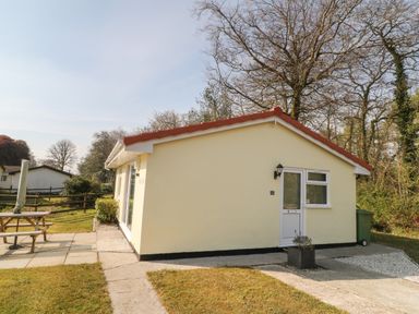 A small yellow house with a red roof and a picnic table outside at Ballasalla in Liskeard