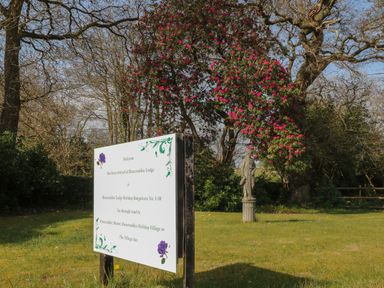 A garden area with a signboard and a statue under a tree with pink flowers at Ballasalla in Liskeard
