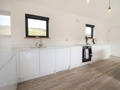 A kitchen with white cabinets a sink an oven two windows and wooden flooring at The Sheep Shed in Llanrhaeadr-Ym-Mochnant