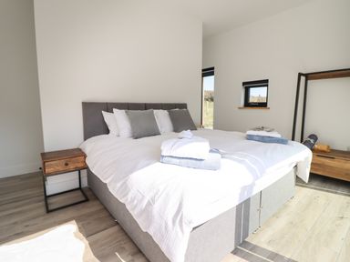 A bedroom with a large bed with white bedding and gray pillows a wooden nightstand and a wooden open closet at The Sheep Shed in Llanrhaeadr-Ym-Mochnant