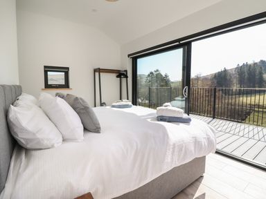 A bedroom with a bed and pillows next to a large window with a view of trees and hills at The Sheep Shed in Llanrhaeadr-Ym-Mochnant