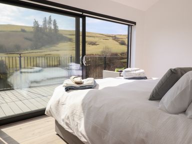 A bedroom with a bed near large glass sliding doors overlooking a balcony and countryside at The Sheep Shed in Llanrhaeadr-Ym-Mochnant