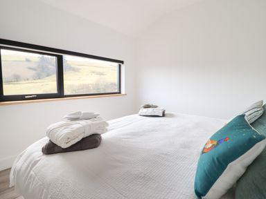 A bedroom with a large bed towels and robes on the bed and a window showing a landscape at The Sheep Shed in Llanrhaeadr-Ym-Mochnant
