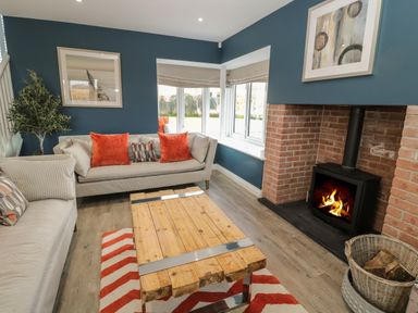 A living room with two sofas orange cushions a wooden coffee table a fireplace and a wicker basket for firewood at The Deck House in Beadnell