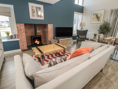 A living room with a wood stove fireplace a striped sofa a wooden coffee table and a television at The Deck House in Beadnell