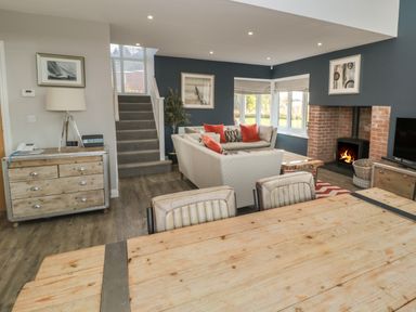 An open plan living room and dining area with a wooden dining table chairs sofas fireplace and staircase at The Deck House in Beadnell