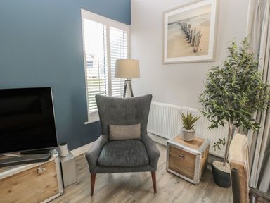 A corner of a living room with a gray armchair and a television on a wooden trunk at The Deck House in Beadnell