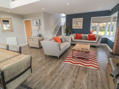 A living room with two sofas red pillows wooden coffee table and dining table at The Deck House in Beadnell