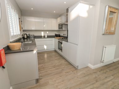 A kitchen with white cabinets wooden floor a sink kettle toaster and oven at The Deck House in Beadnell