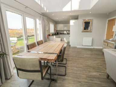 A dining area with a wooden table and chairs next to glass doors and a kitchen in the background at The Deck House in Beadnell