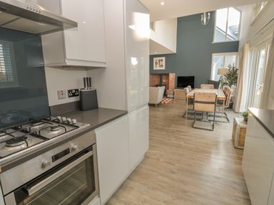 A kitchen with a gas stove and oven opening into a dining area with a wooden table and chairs at The Deck House in Beadnell