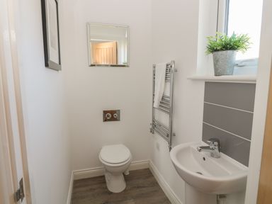 A small bathroom with a toilet a sink a towel rack a mirror and a plant on the windowsill at The Deck House in Beadnell