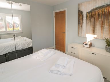 A bedroom with a bed with folded towels a wooden door a white cabinet a radio a plant and a painting at The Deck House in Beadnell