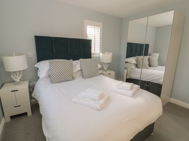 A bedroom with a bed with pillows and folded towels next to bedside tables with lamps and a mirrored wardrobe at The Deck House in Beadnell