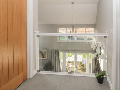 A hallway with a wooden door a glass railing a potted plant and a view to a room with patio doors and outdoor furniture at The Deck House in Beadnell