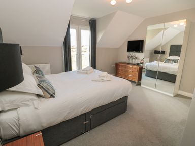 A bedroom with a bed towels on the bed wooden dresser mirror wardrobe and double glass doors at The Deck House in Beadnell