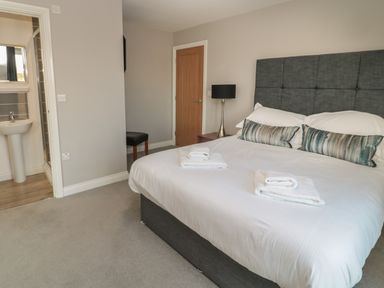 A bedroom with a double bed, bedside table with lamp, chair, and an ensuite bathroom at The Deck House in Beadnell