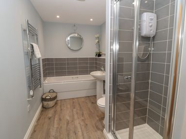 A bathroom with a bathtub sink toilet shower and round mirror at The Deck House in Beadnell