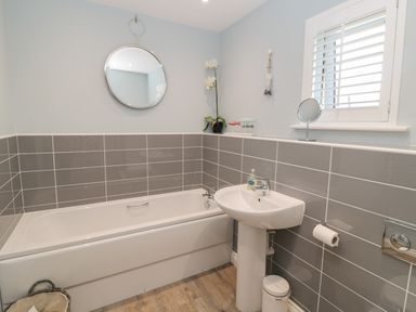 A bathroom with a bathtub sink round mirror and window with shutters at The Deck House in Beadnell