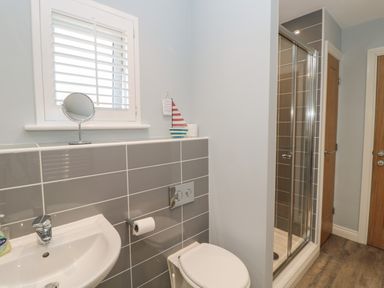 A bathroom with a sink a toilet a shower with glass doors and a window with shutters at The Deck House in Beadnell