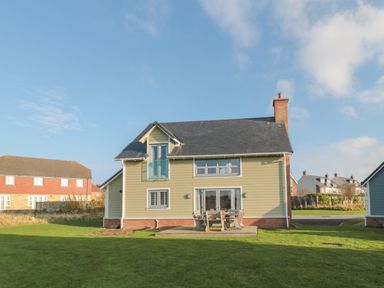 A two-story house with a patio table and chairs on a lawn at The Deck House in Beadnell