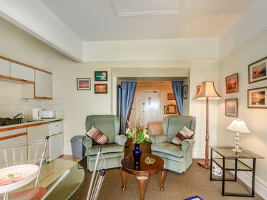 A sitting area with two armchairs and a coffee table with flowers and a kitchen area with cabinets and appliances at Clooneavin Apartment 4 in Lynmouth